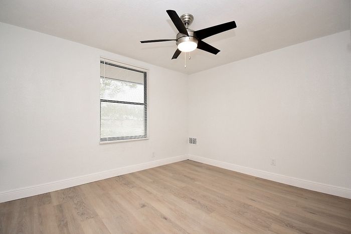 Bright and airy bedroom with elegant hardwood flooring, sleek ceiling fan, and ample natural light through a large window.