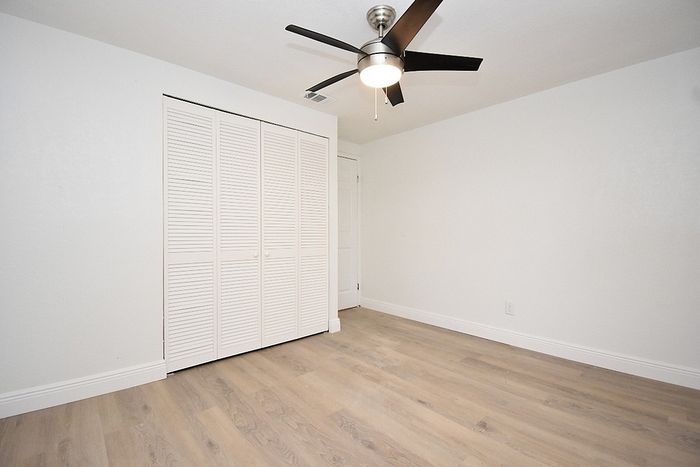 Bright and inviting room with sleek hardwood floors, modern ceiling fan, and ample closet space with white paneled doors.