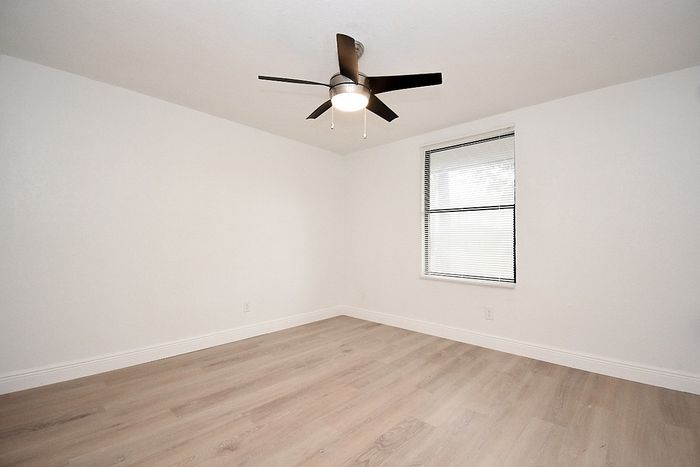 Bright and airy room with sleek hardwood floors and a modern ceiling fan, ideal for a cozy bedroom or stylish office.