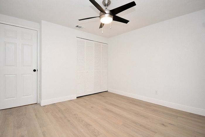 Spacious and bright room with modern ceiling fan and elegant wood flooring, ideal for a cozy bedroom setup.