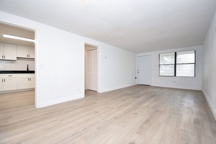 Bright and spacious living area with modern hardwood floors, adjacent to a sleek kitchen featuring pristine cabinets and ample counter space.