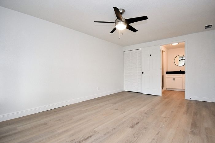 Spacious bedroom with elegant wood flooring, modern ceiling fan, and a stylish ensuite bathroom.