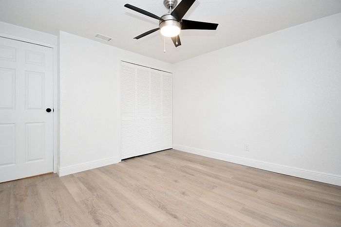 Bright, modern bedroom featuring sleek laminate flooring, a stylish ceiling fan, and ample closet space.