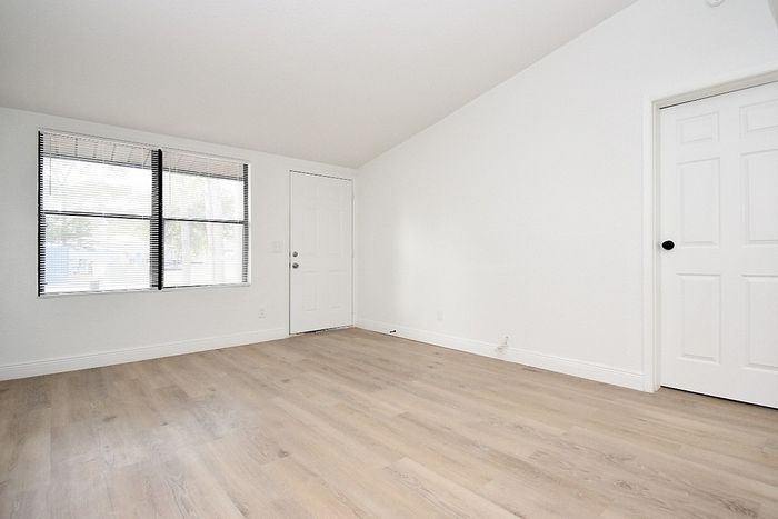 Bright, airy room with large window, sleek hardwood flooring, and modern white finishes, perfect for customizable living.