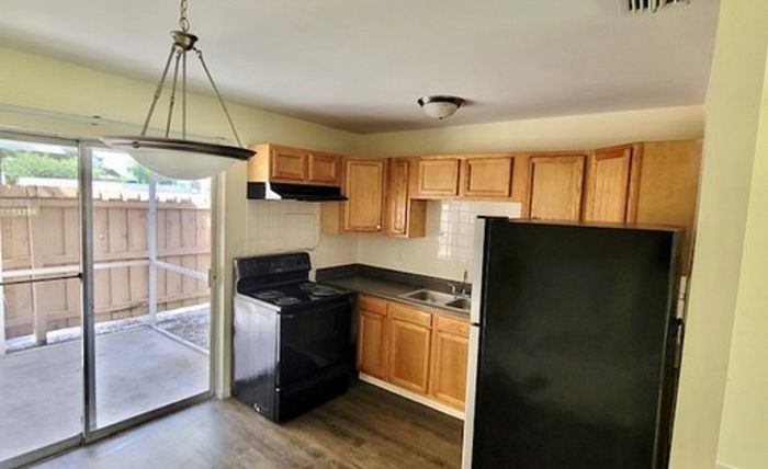 Charming apartment kitchen with wooden cabinets, modern black appliances, and a sliding glass door that opens to a private outdoor space.
