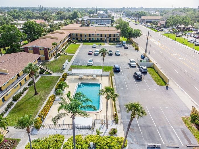 Inviting aerial view of a charming apartment complex with well-maintained outdoor pool, lush green spaces, and ample parking, set in a serene neighborhood.