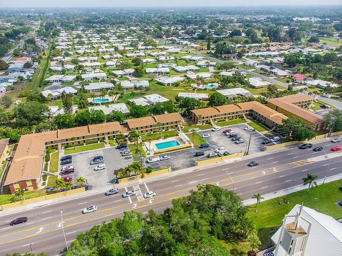 Aerial view of a picturesque apartment complex with inviting pool, ample parking, and lush green surroundings in a tranquil neighborhood.