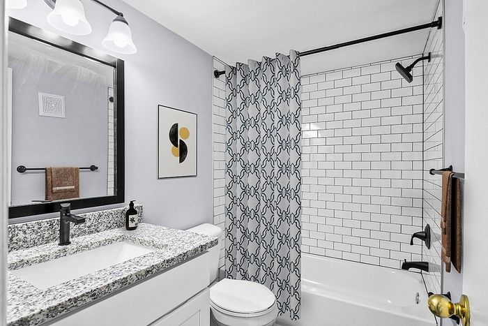 Chic bathroom with elegant granite countertop, stylish black fixtures, and modern patterned shower curtain.