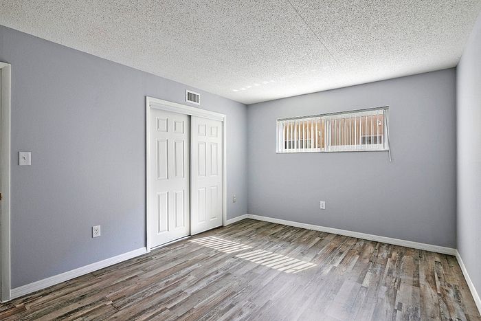 Bright and inviting bedroom with modern grey walls, sleek wood flooring, and ample natural light from a wide window.