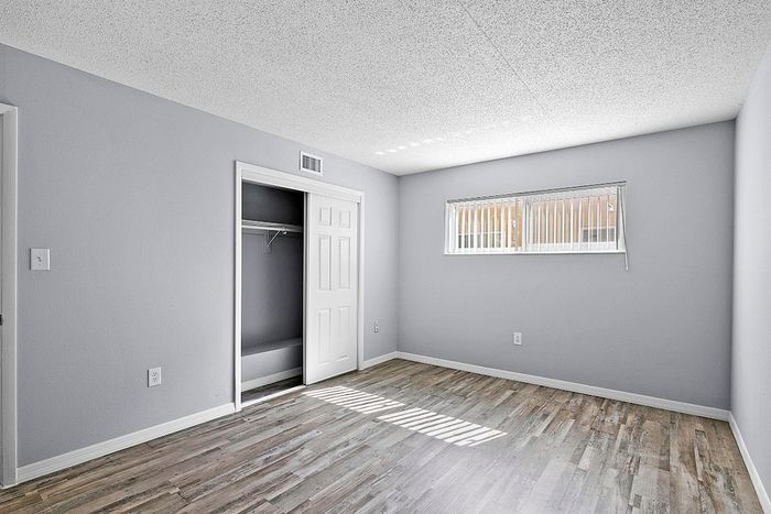 Bright and inviting bedroom with elegant wooden flooring, ample natural light through a large window, and a spacious open closet.