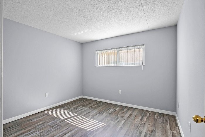 Bright and airy bedroom with sleek hardwood flooring, featuring a large window allowing natural light to enhance the spacious feel.