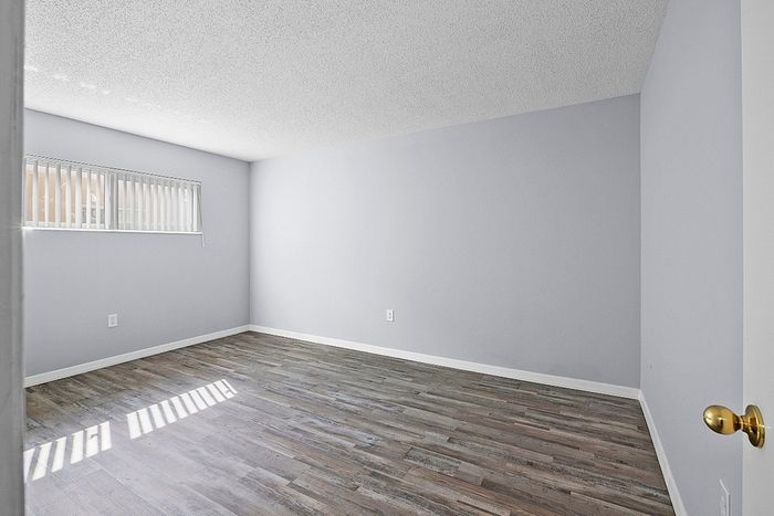 Bright and airy room with elegant wood flooring and a large window, perfect for a cozy bedroom or home office.