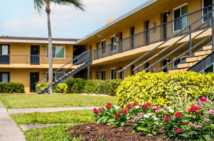 Charming apartment complex with vibrant landscaping, featuring lush greenery and colorful flowers against a sunny backdrop.