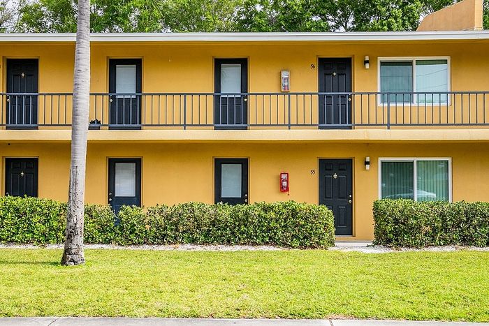 Charming two-story apartment exterior with vibrant yellow facade, private balconies, and lush green landscaping.