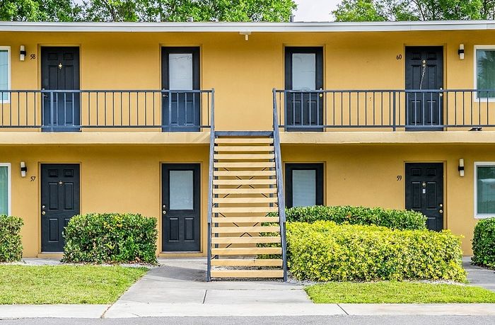 Charming two-story apartment complex with vibrant yellow exterior, featuring secure dark doors, lush greenery, and a welcoming staircase.