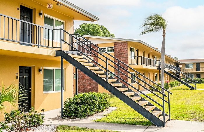 Charming apartment building with vibrant yellow exteriors, convenient outdoor staircases, and lush green surroundings.