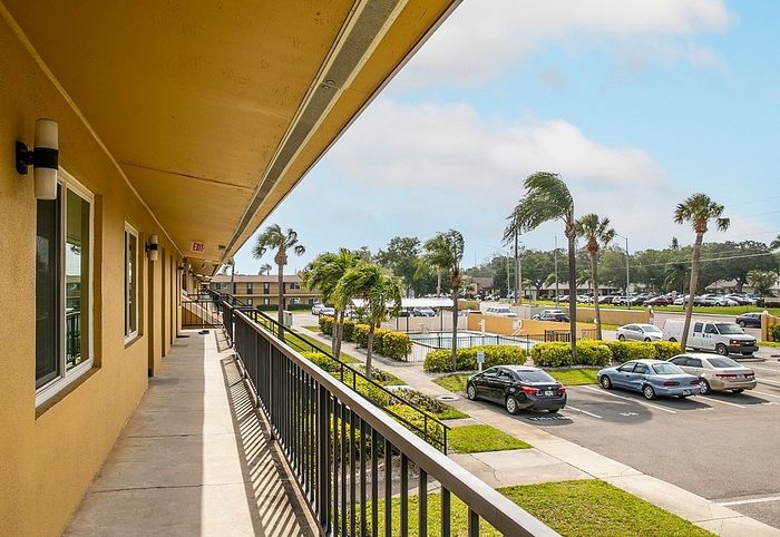Inviting apartment exterior with a sunny walkway, palm trees, and ample parking, offering a tropical vibe.