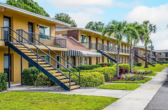 Charming apartment complex with inviting staircases, lush greenery, and vibrant palm trees, offering a tropical getaway vibe.