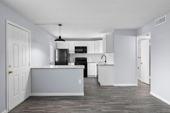 Modern kitchen with sleek white cabinets, a black refrigerator, and stylish pendant lighting, showcasing an open-plan layout with elegant grey flooring.