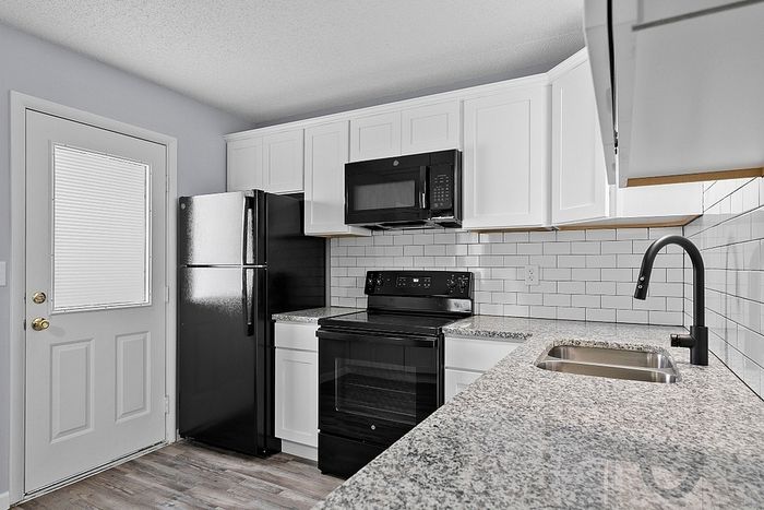 Modern kitchen with sleek black appliances, white cabinetry, and stylish granite countertops.