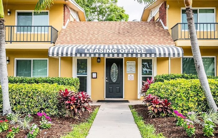 Inviting leasing office entrance with vibrant landscaping and welcoming striped awning.