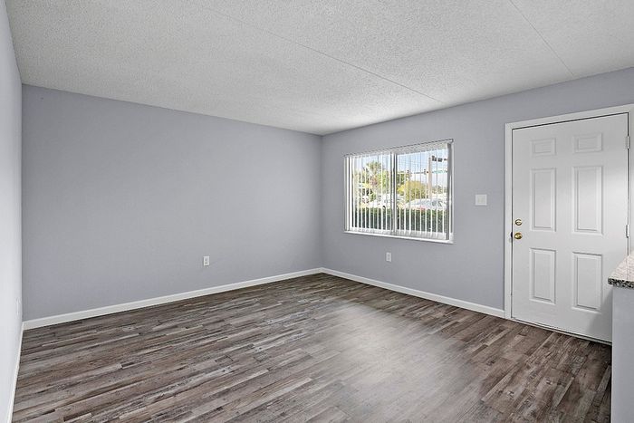 Inviting living space with modern wooden flooring, ample natural light from large window, and neutral walls, ready for personalization.