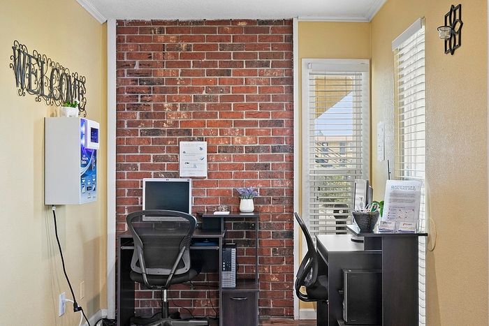 Inviting home office space featuring a stylish brick accent wall, a welcoming 'Welcome' sign, and ample natural light from adjacent windows.