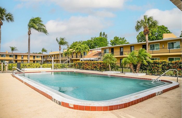 Inviting apartment complex with a sparkling swimming pool surrounded by lush palm trees and vibrant landscaping, perfect for relaxation.