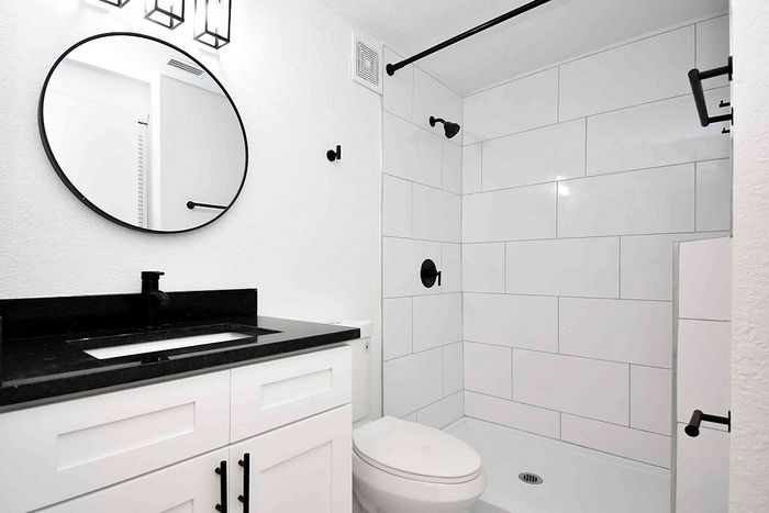 Sleek modern bathroom featuring a stylish black and white design with a spacious walk-in shower and elegant circular mirror.