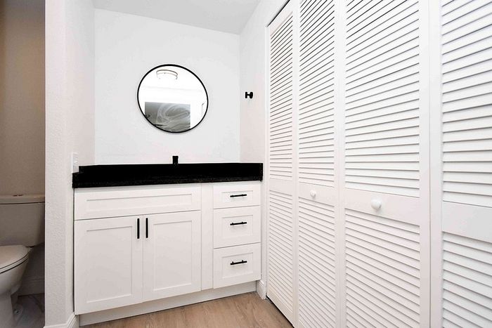 Modern bathroom with sleek white cabinets, a polished black countertop, and a stylish round mirror for a contemporary touch.