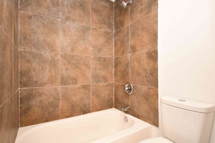 Modern bathroom featuring elegant brown tiled walls, a pristine white bathtub, and a sleek toilet, offering a relaxing and functional space.