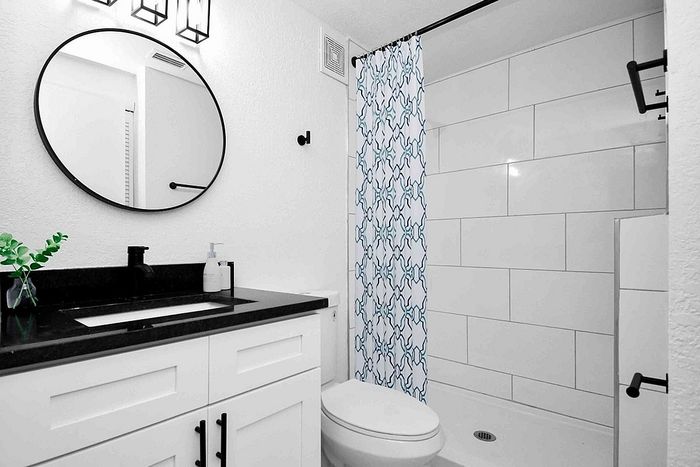 Contemporary bathroom design featuring sleek black countertops, chic round mirror, and elegant tiled shower with modern geometric curtain.