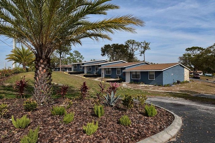 Charming blue duplex apartments with manicured landscaping and palm trees, nestled in a serene suburban setting.