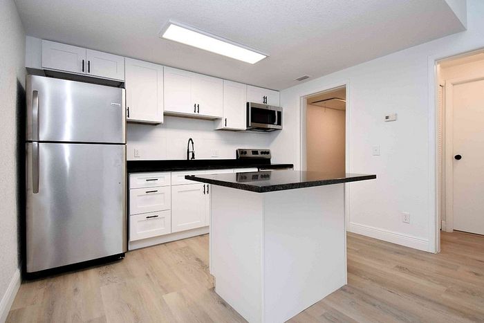 Modern kitchen with sleek stainless steel appliances, elegant white cabinetry, and a stylish central island on polished wood flooring.