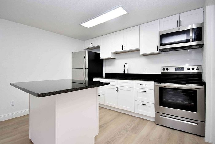 Modern kitchen with sleek white cabinetry, stainless steel appliances, and a chic black granite island.
