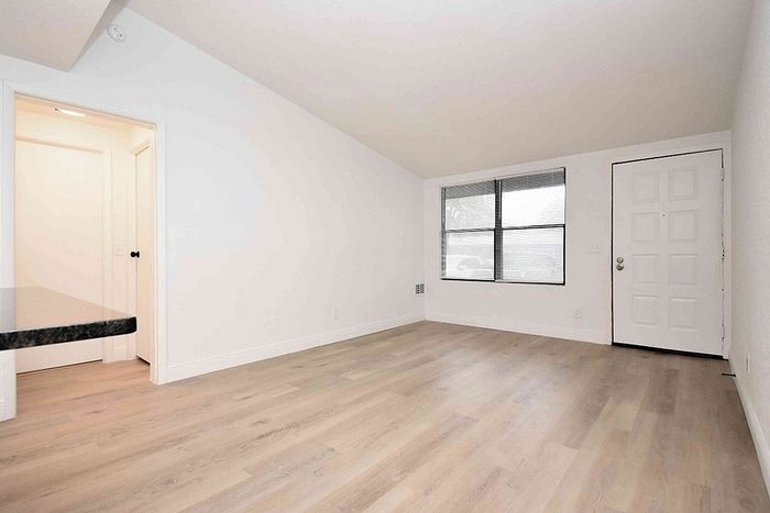 Bright and airy living area with elegant wooden flooring, large window for natural light, and fresh white walls.