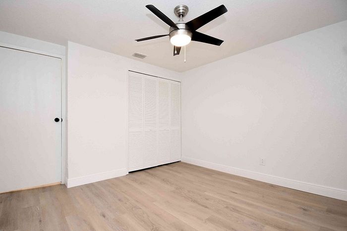 Bright, airy room with elegant light-colored wood flooring, sleek ceiling fan, and ample closet space.
