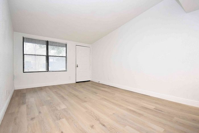 Bright and spacious room featuring elegant wood flooring and large windows, perfect for a cozy living area.