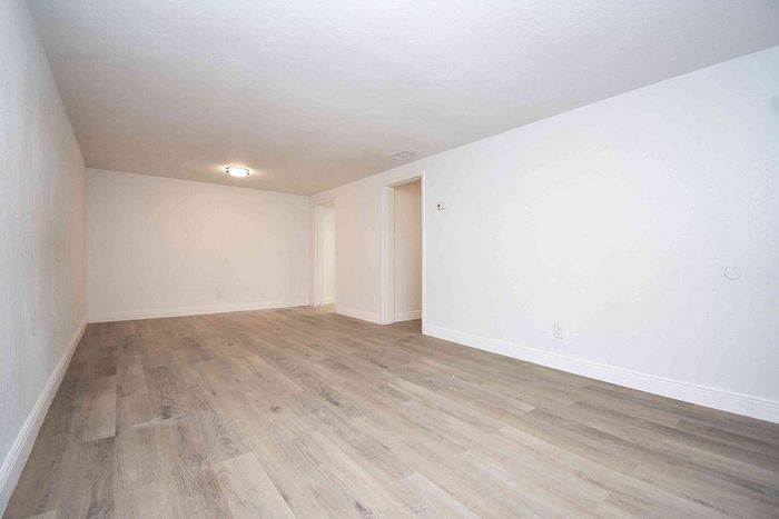 Spacious and bright room with sleek wooden flooring and modern light fixture, perfect for versatile living arrangements.