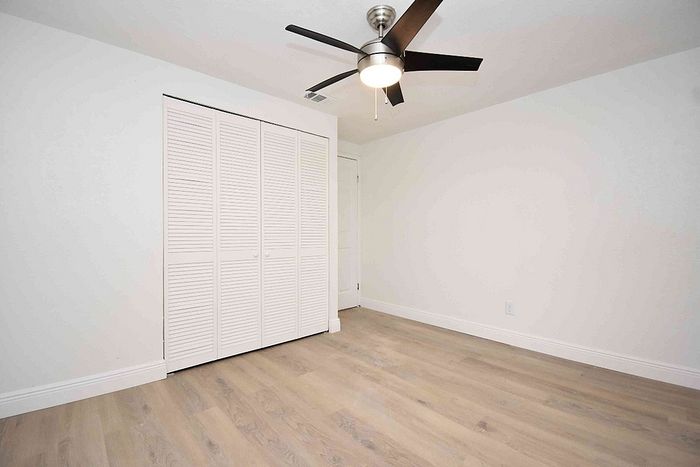 Bright and inviting bedroom with sleek wood flooring, a ceiling fan, and ample closet space with white louvered doors.