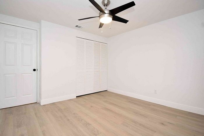 Bright and airy bedroom with modern ceiling fan and sleek hardwood flooring, perfect for a serene retreat.