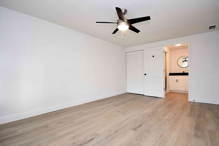 Spacious bedroom with sleek ceiling fan, warm wood flooring, and modern en-suite bathroom.