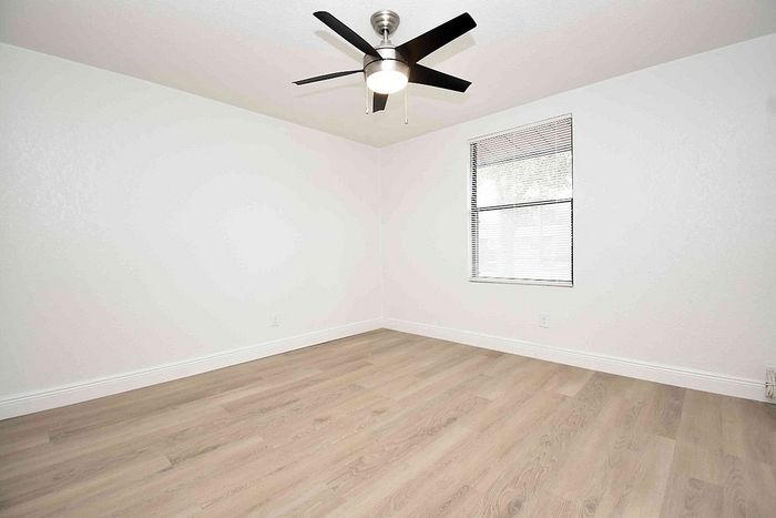 Bright and airy room with elegant hardwood floors, modern ceiling fan, and large window for natural light.