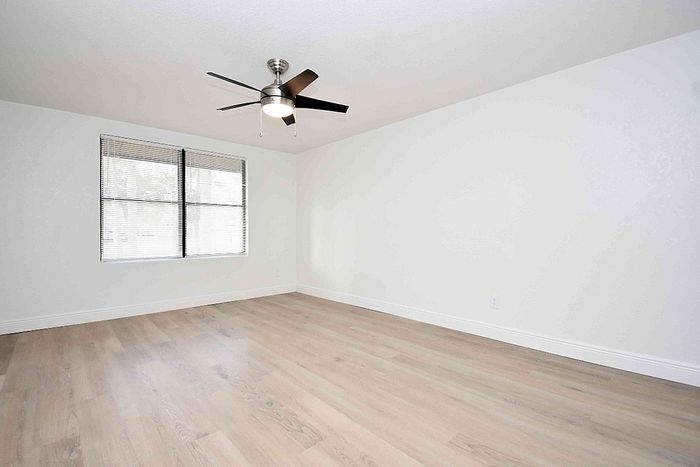 Bright and spacious room with sleek hardwood flooring and modern ceiling fan, ideal for a serene bedroom.