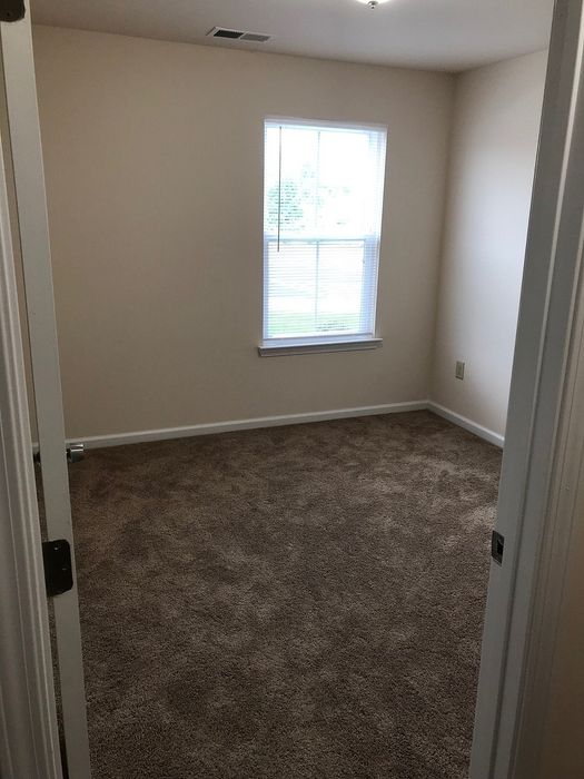 Cozy bedroom with plush carpeting and abundant natural light from a large window, perfect for a serene personal retreat.