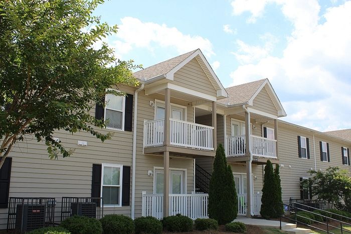 Charming two-story apartment building with cozy balconies, surrounded by lush greenery and vibrant trees.