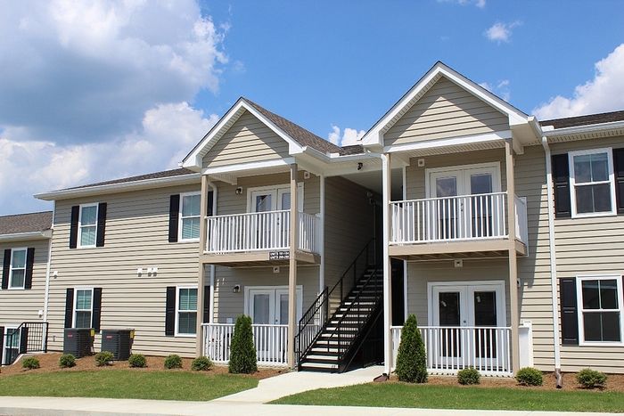 Charming modern apartment complex with two levels, featuring spacious balconies and a sleek exterior design against a bright blue sky.
