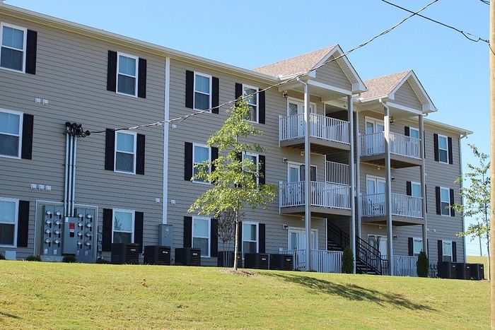 Modern apartment building with spacious balconies, surrounded by lush greenery and clear blue skies, offering a serene living experience.