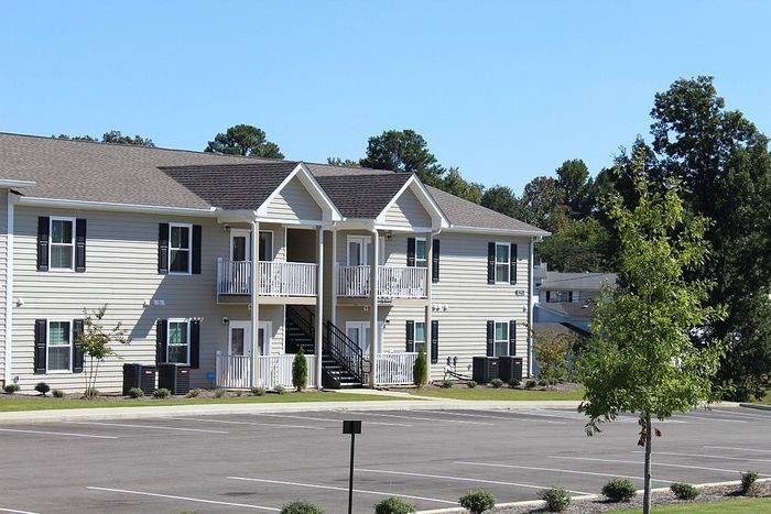 Charming modern apartment building with central balconies, surrounded by lush greenery and ample parking space.