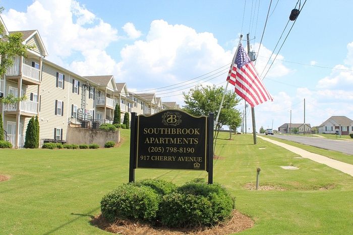 Inviting exterior view of Southbrook Apartments with well-maintained lawns and a vibrant American flag, offering a serene living environment.